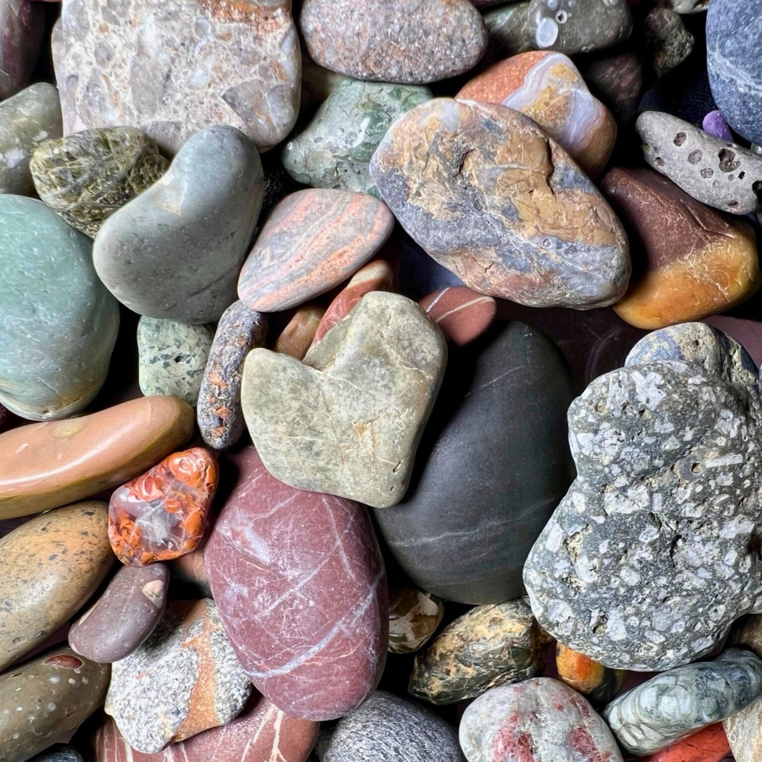 Close up of a green heart shaped stone laying on a pile of sea pebbles