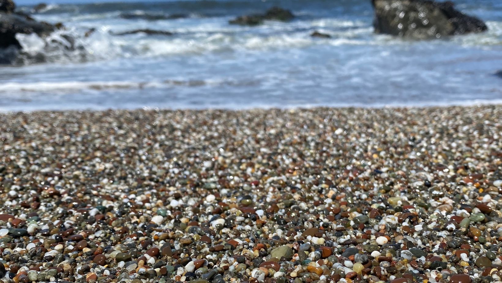 Close up of wet beach stones at the shoreline and ocean in the background